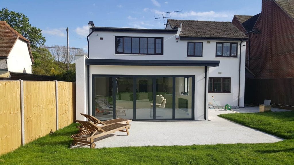 White rendered two-storey house with large dark-framed windows and a lawn
