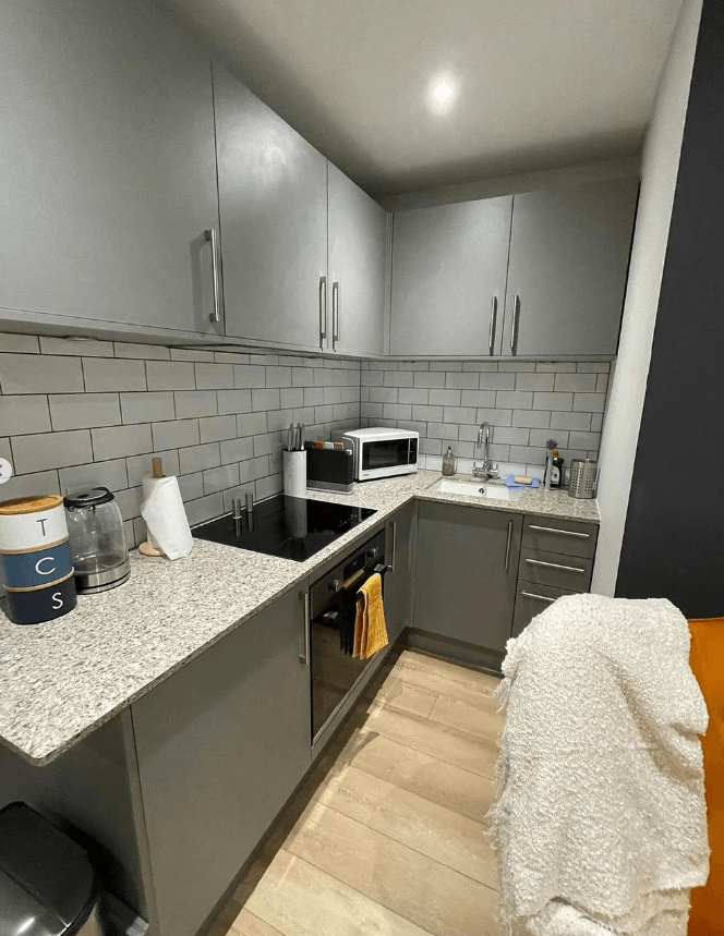 Kitchen with dark green units, a stone worktop and an oak floor